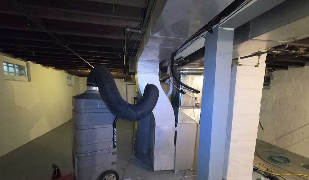 Air duct cleaning vacuum attached to a furnace in the basement.