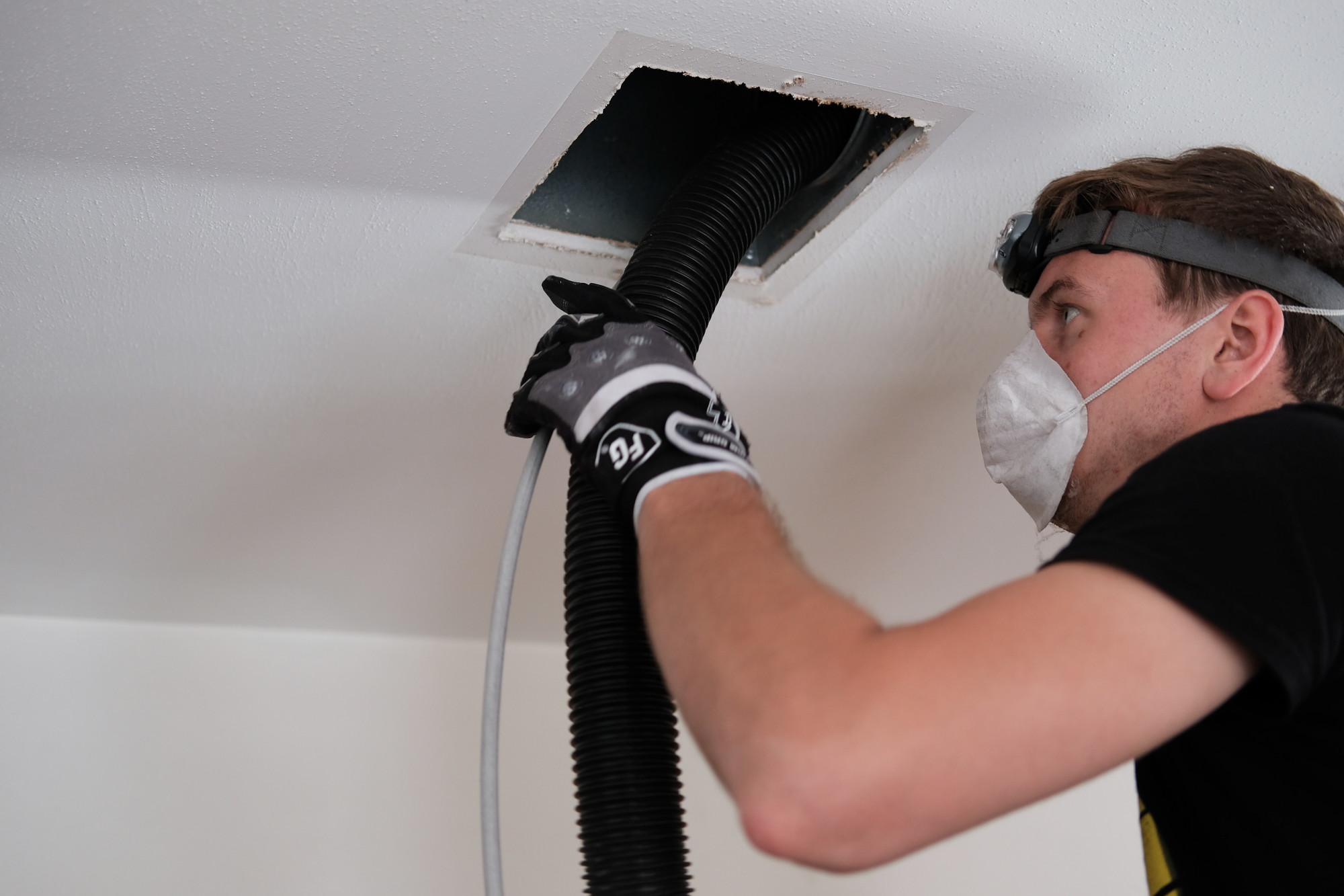 A technician cleaning air ducts in a ceiling.