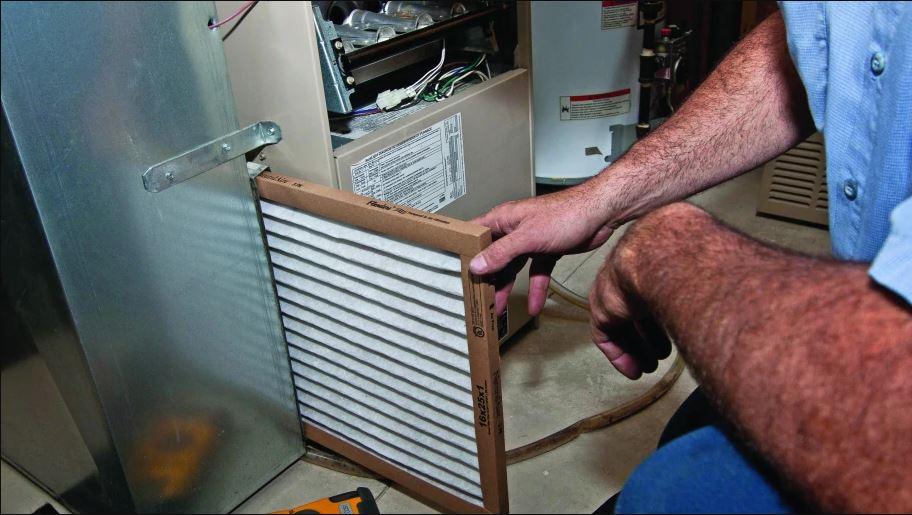 HVAC technician doing maintenance on a furnace and replacing the filter.