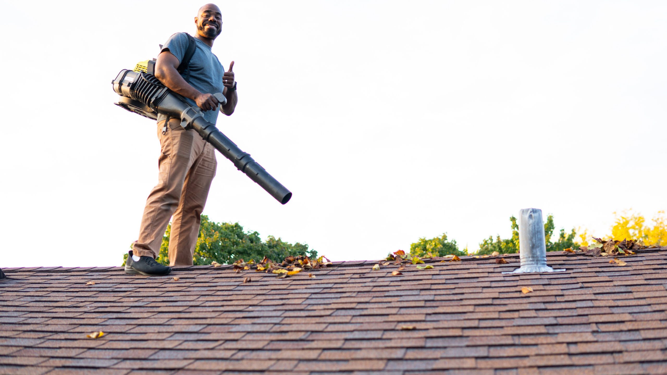 Professional on a roof cleaning gutters with his leaf blower.